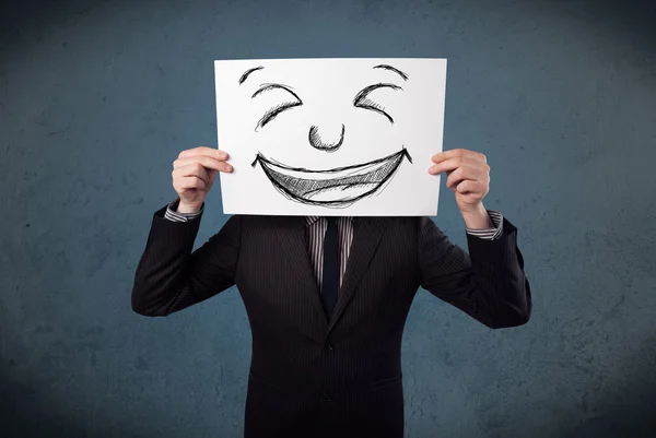 Businessman holding a paper with smiley face in front of his hea — Stock Photo, Image