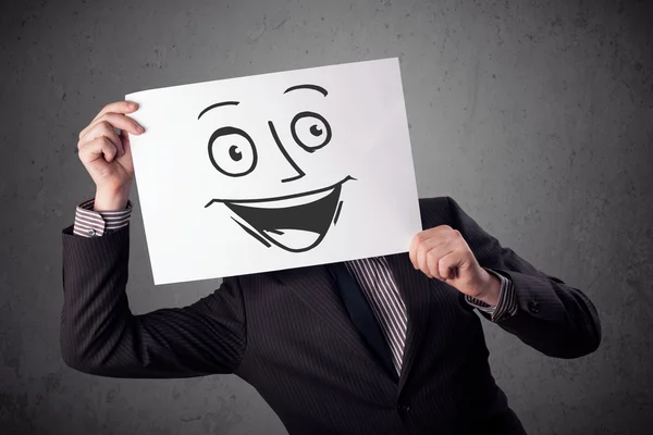 Businessman holding a cardboard with smiley face on it in front — Stock Photo, Image