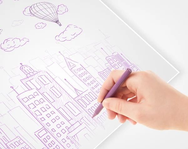 Een persoon die het tekenen van de schets van een stad met ballonnen en wolken op een — Stockfoto