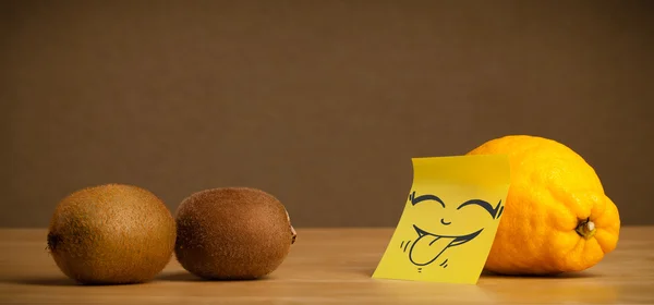 Lemon with post-it note sticking out tongue to kiwis — Stock Photo, Image