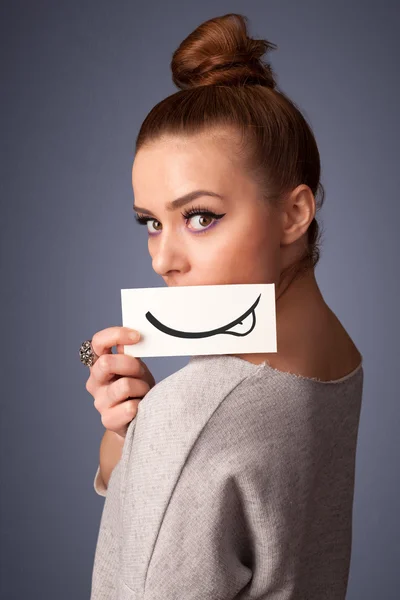Красивая молодая девушка держит белую карточку с рисунком улыбки — стоковое фото