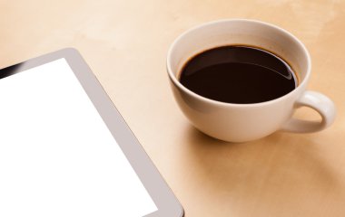 Boş alanı olan bir tablet bilgisayar ve masada bir fincan kahve.