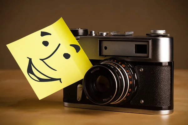 Nota pós-it com rosto sorridente colado em uma câmera fotográfica — Fotografia de Stock