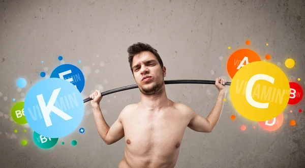 Skinny guy lifting colorful vitamin weights — Stock Photo, Image