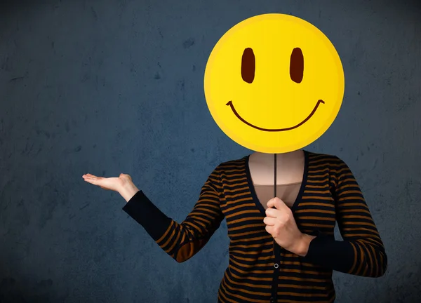 Young woman holding a smiley face emoticon — Stock Photo, Image