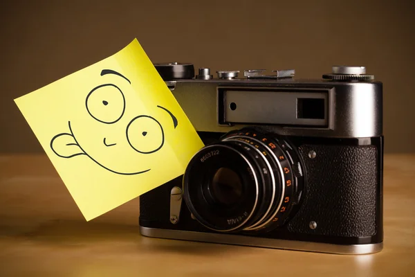 Nota post-it con la cara sonriente pegada a una cámara fotográfica —  Fotos de Stock