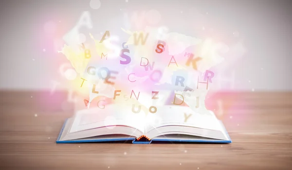 Open book with glowing letters on concrete background — Stock Photo, Image