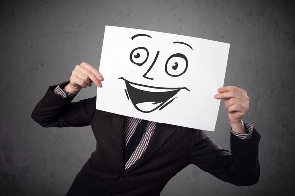 Empresário segurando um papelão com rosto sorridente na frente — Fotografia de Stock