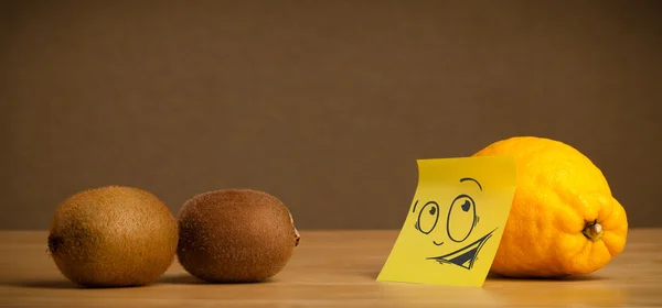 Lemon with post-it note looking curiously at kiwis — Stock Photo, Image