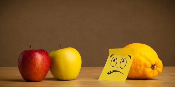 Lemon with sticky post-it note looking sadly at apples — Stock Photo, Image