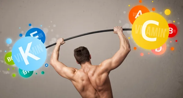 Muscular man lifting colorful vitamin weights — Stock Photo, Image