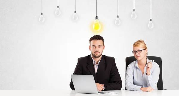 Hombre y mujer de negocios sentados a la mesa con bombillas de idea — Foto de Stock