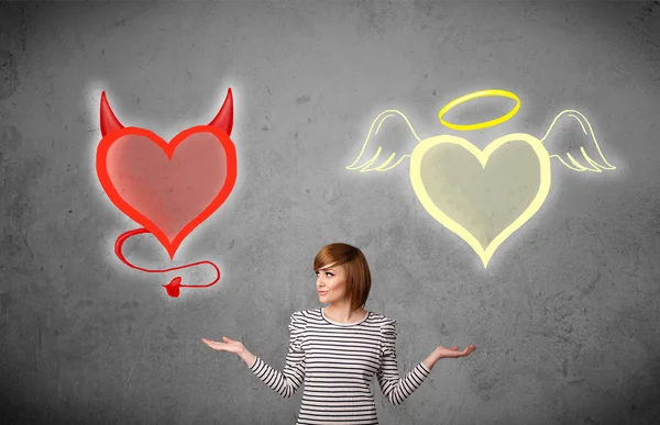 Frau, die zwischen Engel und Teufelsherzen steht — Stockfoto