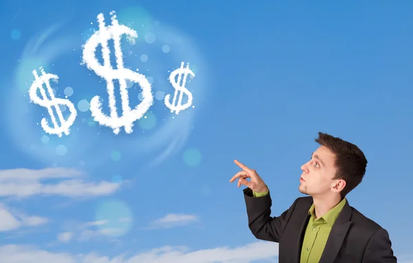 Empresario apuntando a nubes de signo de dólar en el cielo azul — Foto de Stock