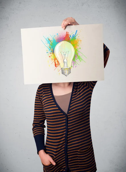 Woman holding a cardboard with paint splashes and lightbulb in f — Stock Photo, Image