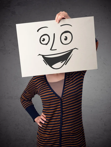 Woman holding a cardboard with smiley face on it in front of her — Stock Photo, Image