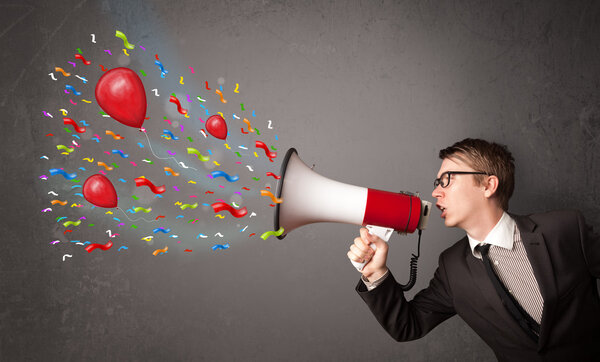 Young guy having fun, shouting into megaphone with balloons 