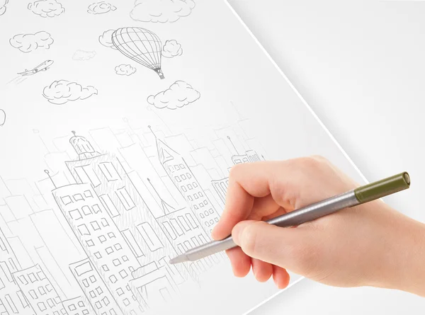 Una persona dibujando bosquejo de una ciudad con globos y nubes en un —  Fotos de Stock