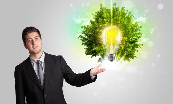 Young man presenting idea light bulb with green tree — Stock Photo, Image