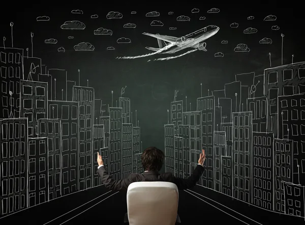 Businessman sitting in front of a cityscape drawing on a chalkbo — Stock Photo, Image