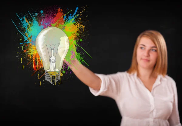 Young lady drawing a colorful light bulb with colorful splashes — Stock Photo, Image