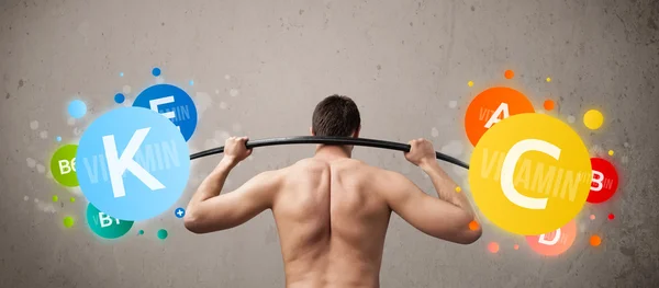 Skinny guy lifting colorful vitamin weights — Stock Photo, Image