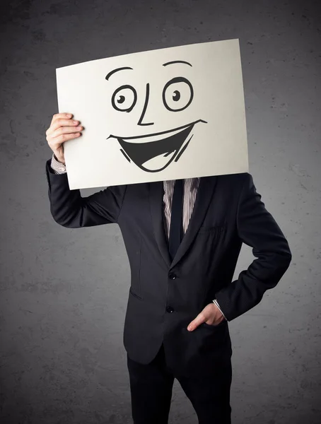Biznesmen trzymając karton z uśmiechniętą twarz to z przodu — Zdjęcie stockowe