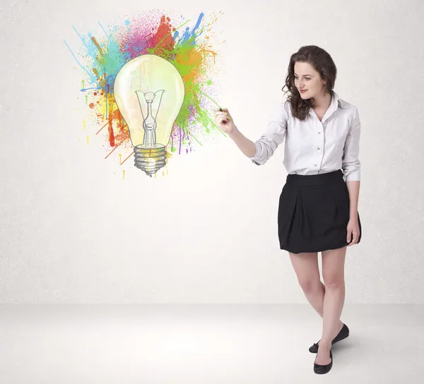 Young lady drawing a colorful light bulb with colorful splashes — Stock Photo, Image