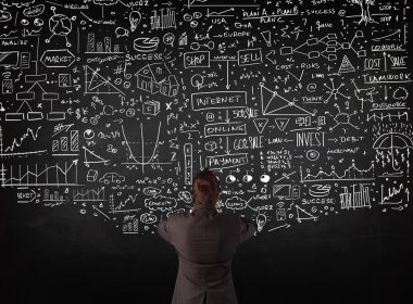 İşadamı tahtaya çizilmiş çizelgelerin önünde duruyor.