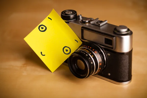 Post-it notera med smiley ansikte klistras på en fotokamera — Stockfoto
