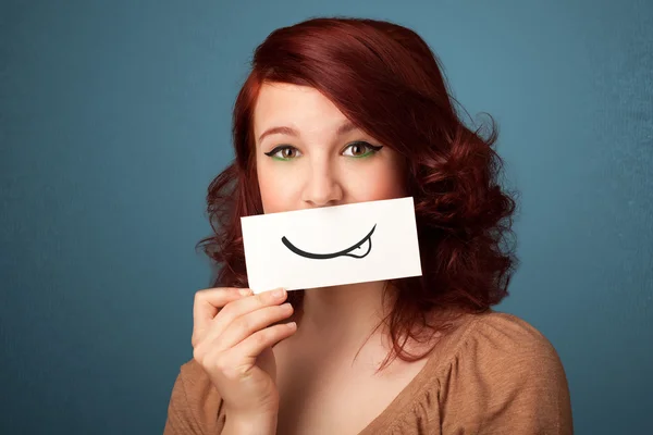 Pretty young girl holding white card with smile drawing — Stock Photo, Image