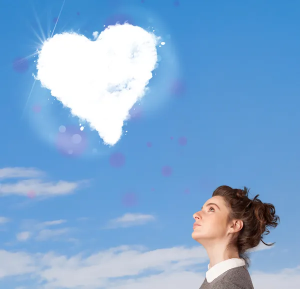 Симпатичная девушка смотрит на белое сердце облако на голубом небе — стоковое фото