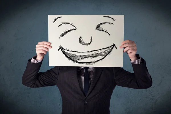 Businessman holding a paper with smiley face in front of his hea — Stock Photo, Image