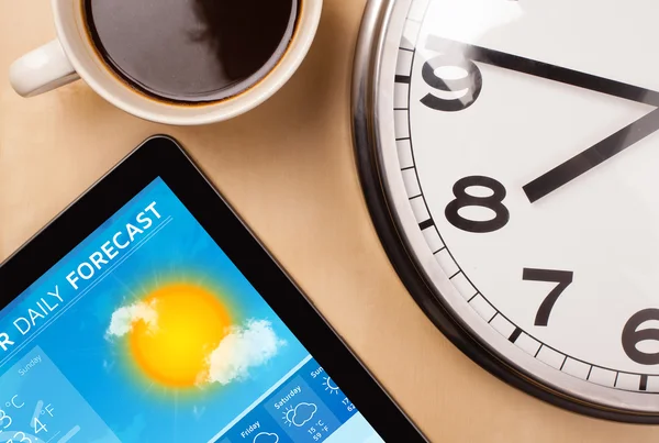 Tablet pc showing weather forecast on screen with a cup of coffe — Stock Photo, Image