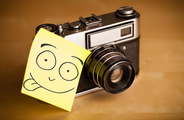 Nota post-it con la cara sonriente pegada a una cámara fotográfica —  Fotos de Stock