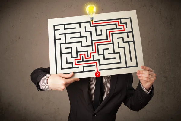 Businessman holding a paper with a labyrinth on it in front of h — Stock Photo, Image