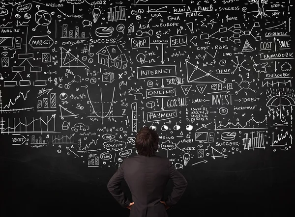 Businessman standing in front of drawn charts on a blackboard — Stock Photo, Image