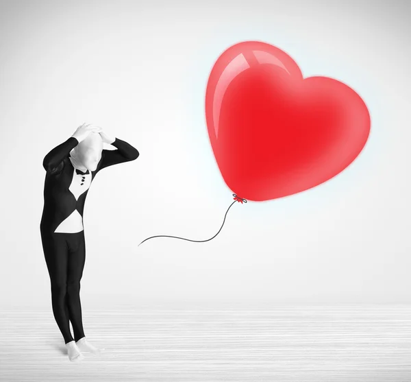 Lindo tipo en traje de cuerpo morpsuit mirando un corazón en forma de globo — Foto de Stock