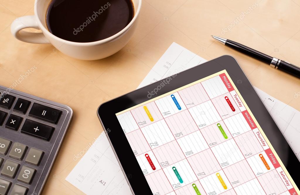 Tablet pc showing calendar on screen with a cup of coffee on a d