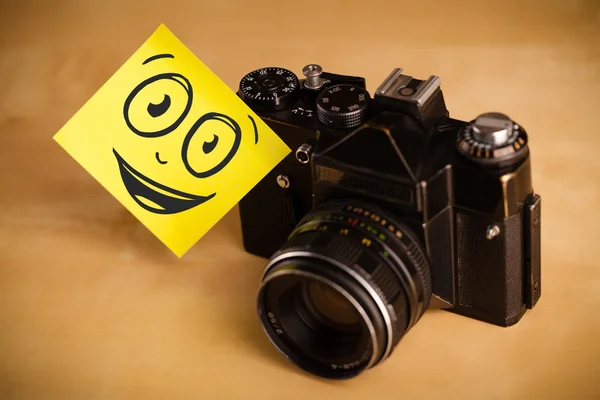 Post-it note with smiley face sticked on photo camera — Stock Photo, Image