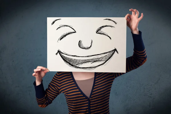 Frau mit gezeichnetem Smiley-Gesicht auf einem Papier vor ihrem Kopf — Stockfoto