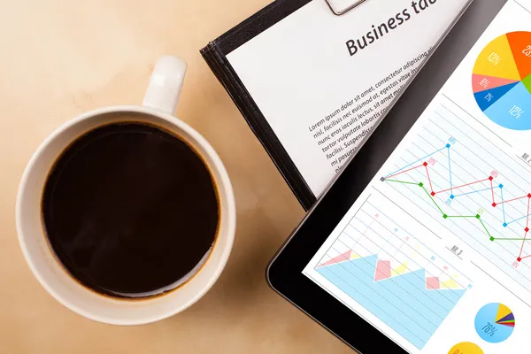 Tablet pc menampilkan grafik pada layar dengan secangkir kopi di atas meja — Stok Foto
