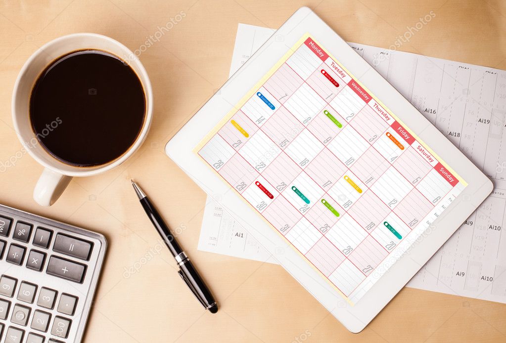 Tablet pc showing calendar on screen with a cup of coffee on a d