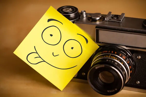 Nota post-it con la cara sonriente pegada a una cámara fotográfica — Foto de Stock