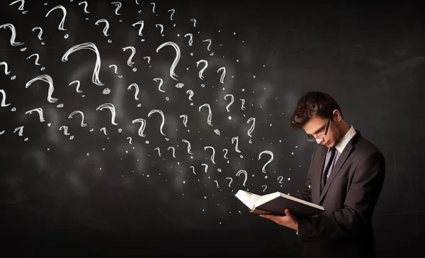 Young man reading a book with question marks coming out from it — Stock Photo, Image