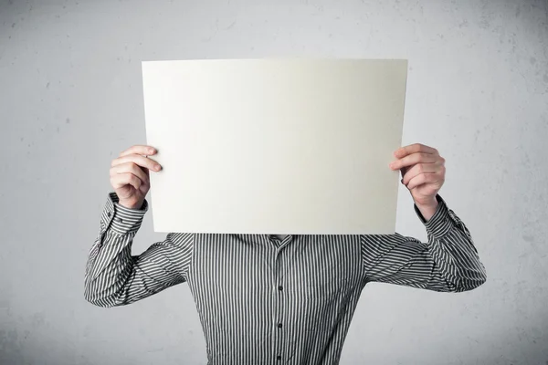 Empresário segurando na frente de sua cabeça um papel com espaço de cópia — Fotografia de Stock