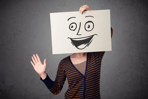 Woman holding a cardboard with smiley face on it in front of her — Stock Photo, Image