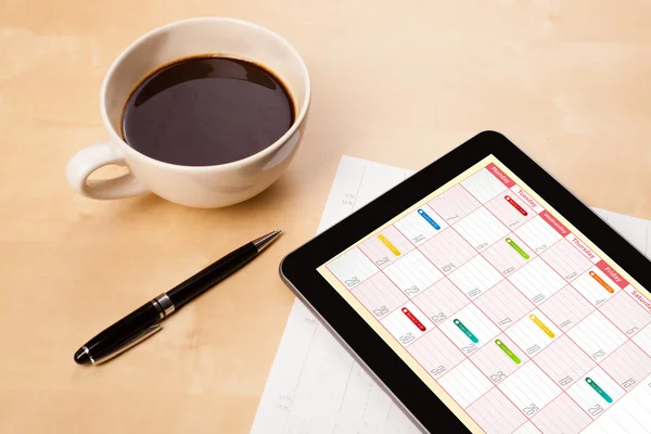 Tablet pc che mostra il calendario sullo schermo con una tazza di caffè su un d — Foto Stock