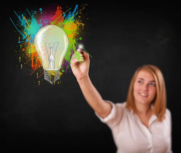 Young lady drawing a colorful light bulb with colorful splashes — Stock Photo, Image