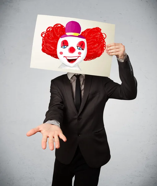 Businessman holding a cardboard with a clown on it in front of h — Stock Photo, Image